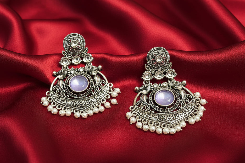 Ornate silver earrings with pearls on a red fabric background