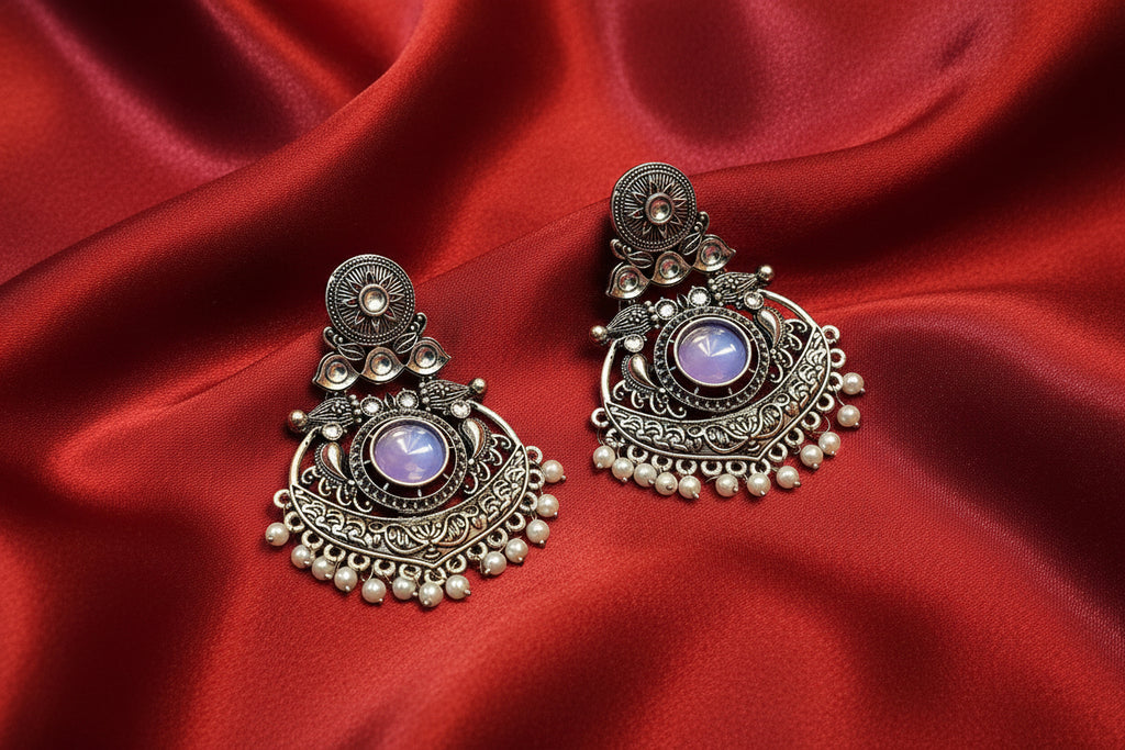 Ornate silver earrings with purple gemstones on a red fabric background