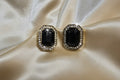 Pair of earrings with black gemstones and gold accents on a satin surface