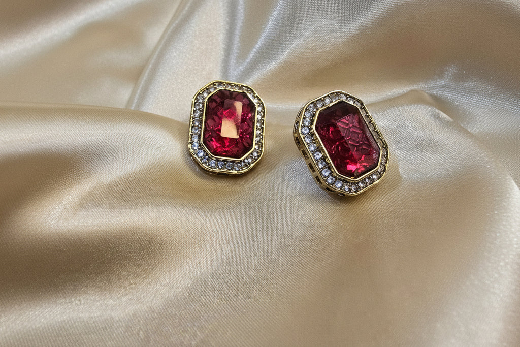 Pair of earrings with red gemstones on a beige satin background