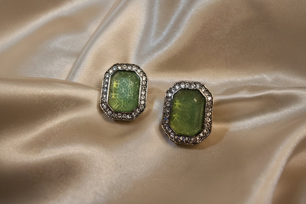 Pair of earrings with green gemstones on a satin surface