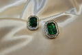 Pair of emerald green gemstone earrings with gold accents on a beige satin background
