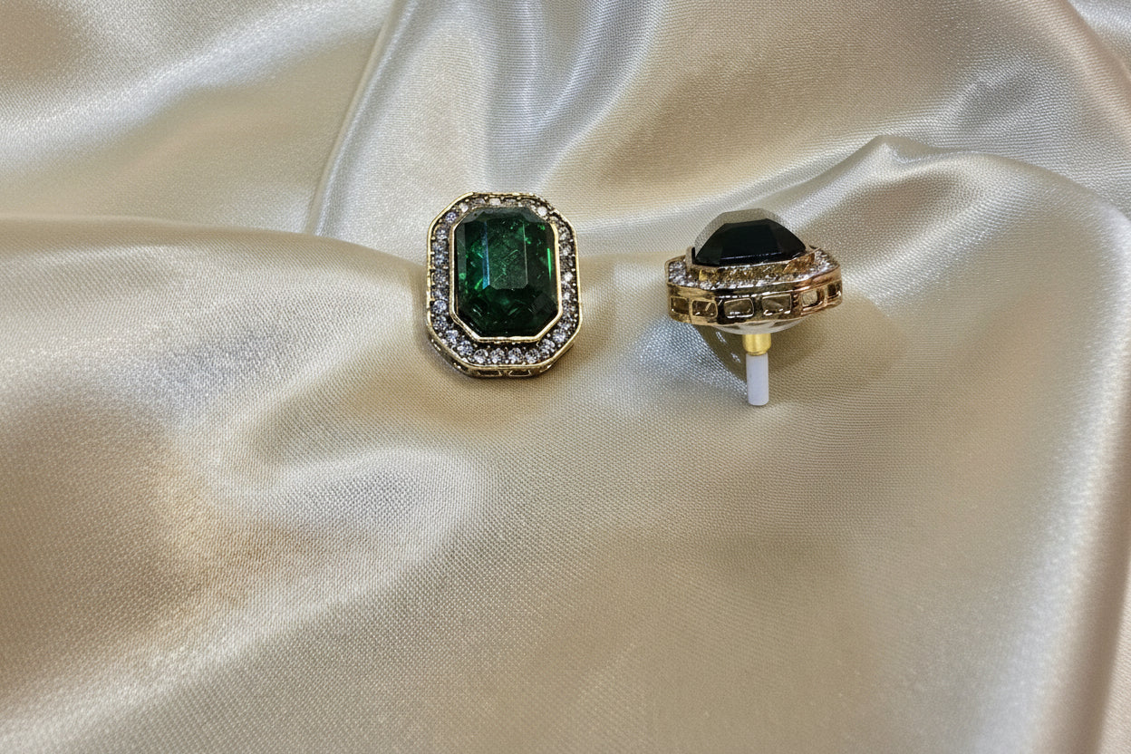 Gold earrings with green gemstones on a beige satin background