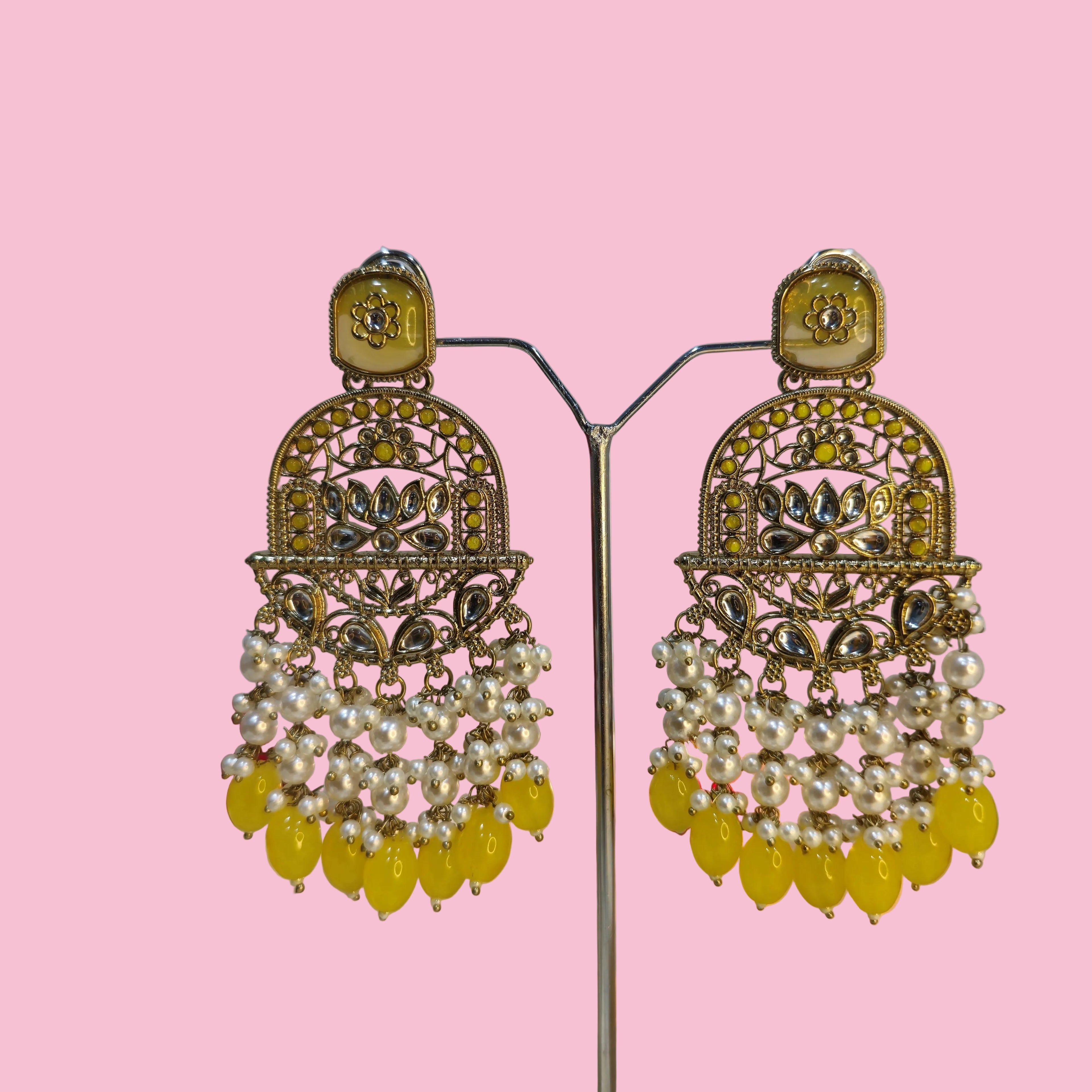 Ornate earrings with yellow and white beads on a reflective surface.
